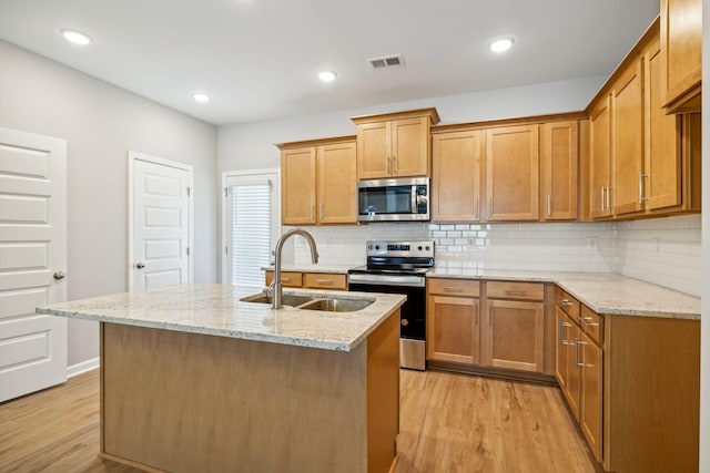 kitchen featuring appliances with stainless steel finishes, an island with sink, a sink, and light stone counters