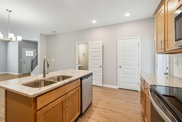 kitchen with pendant lighting, appliances with stainless steel finishes, a kitchen island with sink, a sink, and light stone countertops