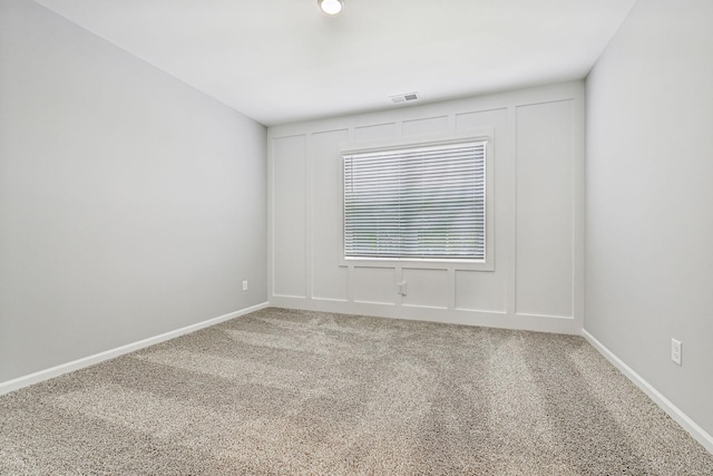 carpeted spare room featuring visible vents, a decorative wall, and baseboards