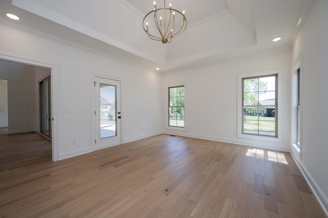 empty room featuring a tray ceiling, a notable chandelier, ornamental molding, wood finished floors, and baseboards