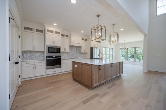 kitchen with white cabinets, a spacious island, glass insert cabinets, stainless steel appliances, and light countertops