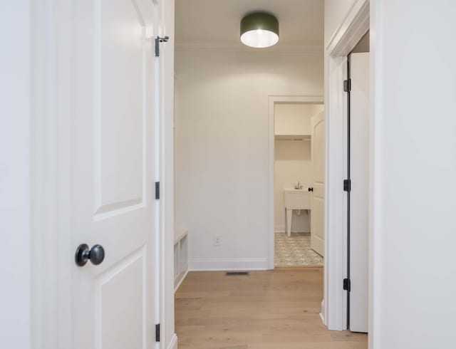 hallway featuring light wood-style floors, baseboards, visible vents, and ornamental molding