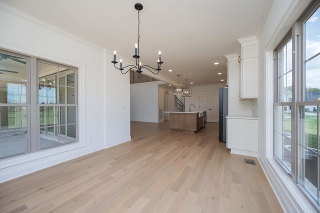 interior space featuring white cabinets, an island with sink, freestanding refrigerator, hanging light fixtures, and an inviting chandelier