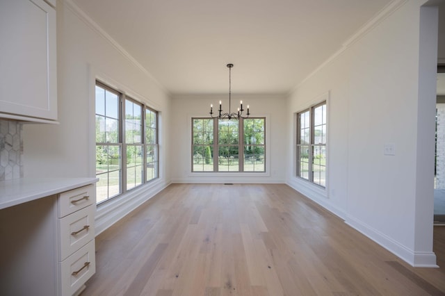 unfurnished dining area featuring light wood-style floors, baseboards, a chandelier, and ornamental molding