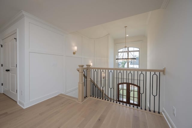 hallway featuring light wood finished floors, crown molding, an upstairs landing, a chandelier, and a decorative wall