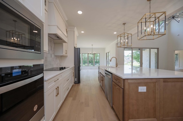 kitchen featuring pendant lighting, black appliances, a kitchen island with sink, and white cabinets