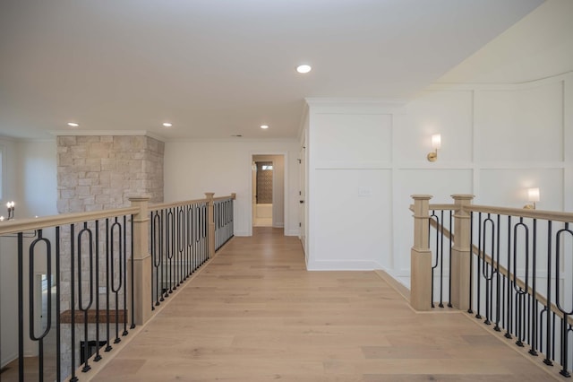 hallway with crown molding, light wood finished floors, recessed lighting, a decorative wall, and an upstairs landing