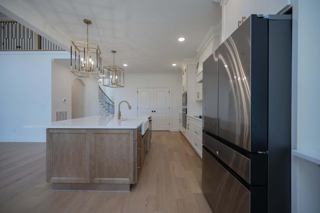 kitchen with a large island with sink, white cabinetry, light countertops, freestanding refrigerator, and decorative light fixtures