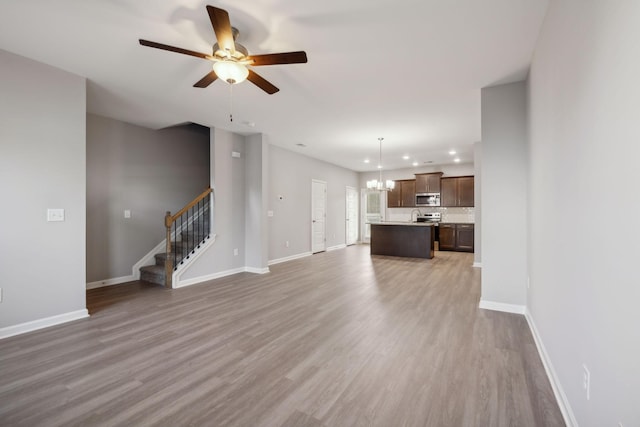 unfurnished living room featuring stairs, recessed lighting, wood finished floors, baseboards, and ceiling fan with notable chandelier