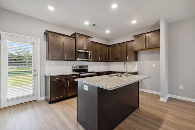 kitchen with a kitchen island with sink, a sink, visible vents, light wood-style floors, and appliances with stainless steel finishes