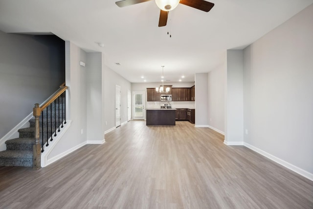 unfurnished living room with light wood-type flooring, baseboards, and stairway