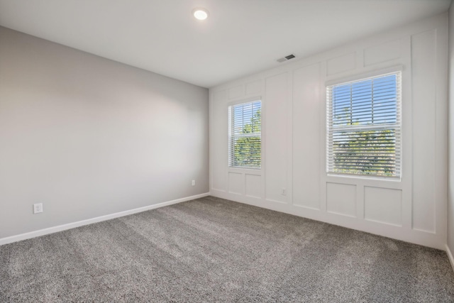 spare room with carpet flooring, a decorative wall, visible vents, and baseboards