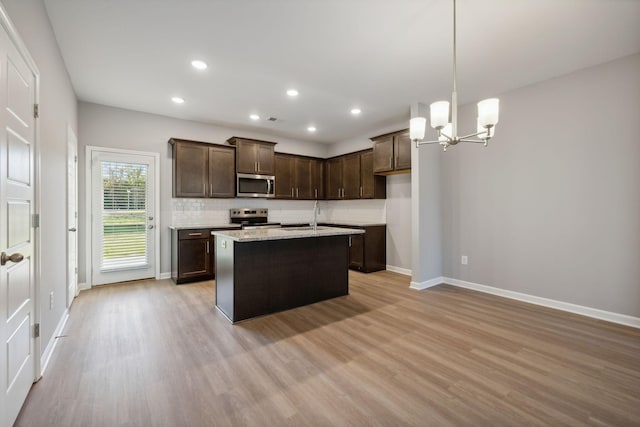 kitchen with light wood-style flooring, a kitchen island with sink, stainless steel appliances, a sink, and pendant lighting