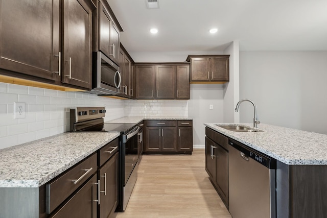 kitchen featuring light wood finished floors, light stone countertops, a kitchen island with sink, stainless steel appliances, and a sink