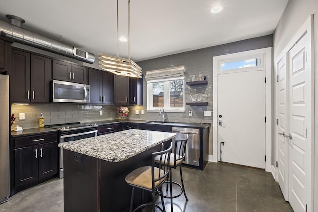 kitchen featuring pendant lighting, stainless steel appliances, a kitchen island, a sink, and dark brown cabinets