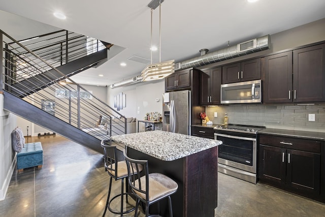 kitchen featuring dark brown cabinetry, stainless steel appliances, a breakfast bar, a kitchen island, and pendant lighting