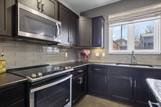 kitchen with stainless steel appliances, tasteful backsplash, a sink, dark stone countertops, and dark brown cabinets