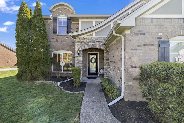 doorway to property featuring stone siding, brick siding, and a lawn