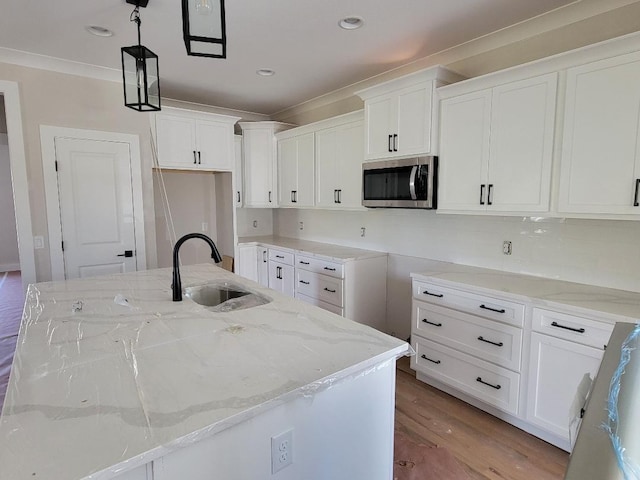 kitchen with a center island with sink, stainless steel microwave, a sink, and decorative light fixtures