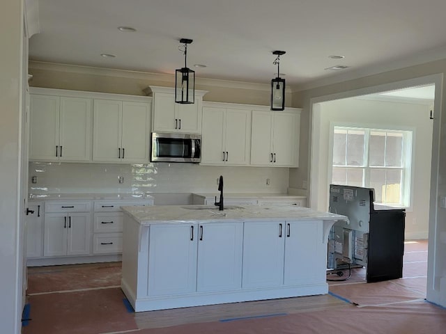 kitchen featuring hanging light fixtures, stainless steel microwave, a center island with sink, and white cabinetry