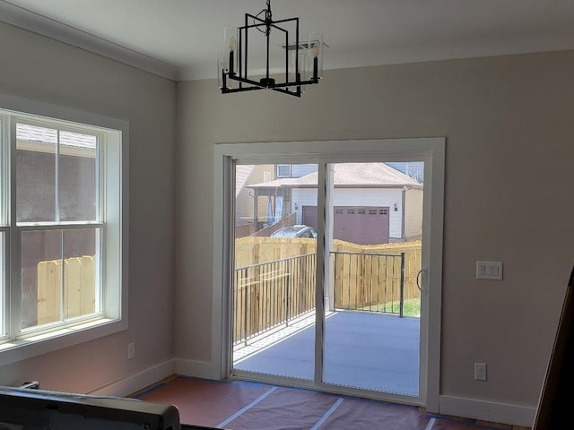 doorway featuring a chandelier, ornamental molding, baseboards, and a healthy amount of sunlight