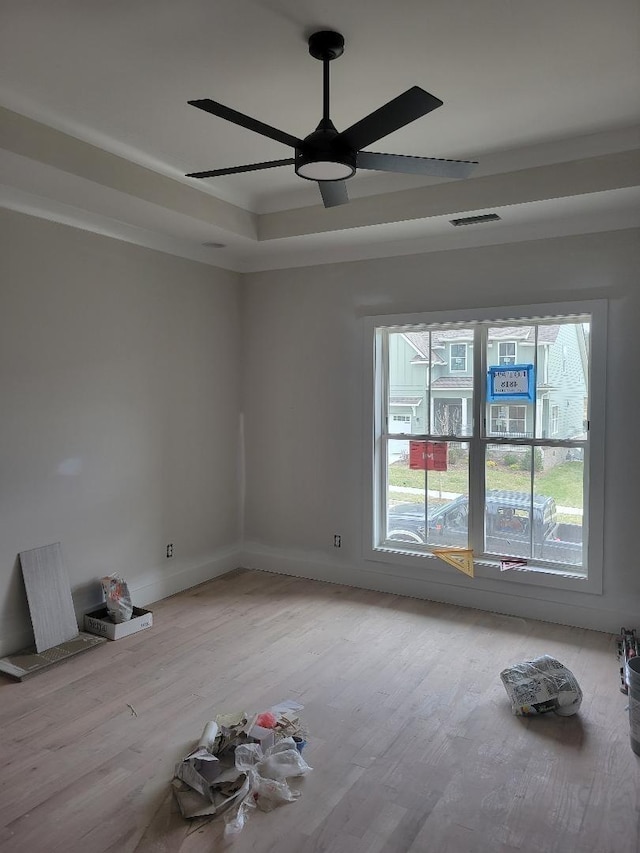 unfurnished room with a raised ceiling, visible vents, ceiling fan, and light wood-style flooring