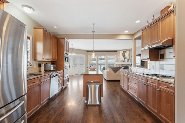 kitchen featuring an island with sink, open floor plan, decorative light fixtures, stainless steel appliances, and under cabinet range hood