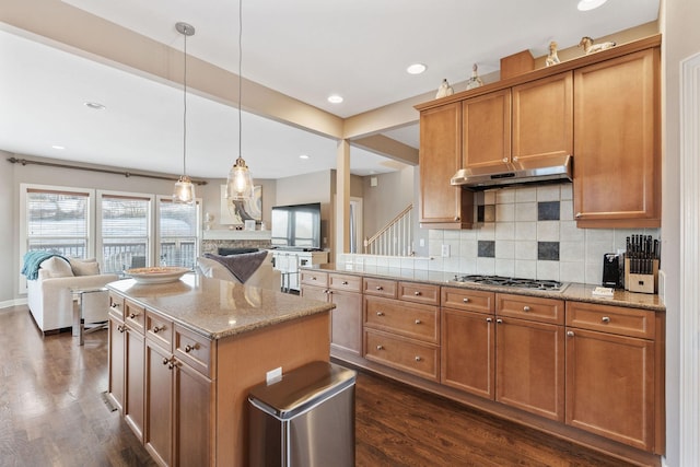 kitchen featuring open floor plan, under cabinet range hood, stainless steel gas stovetop, and pendant lighting