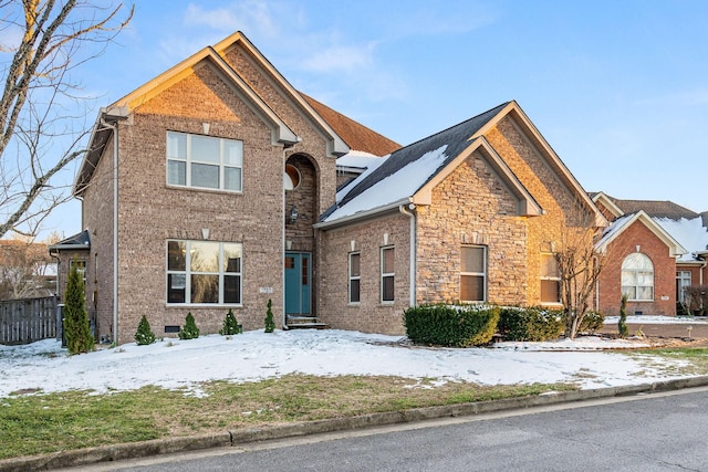 traditional home featuring stone siding, fence, and brick siding