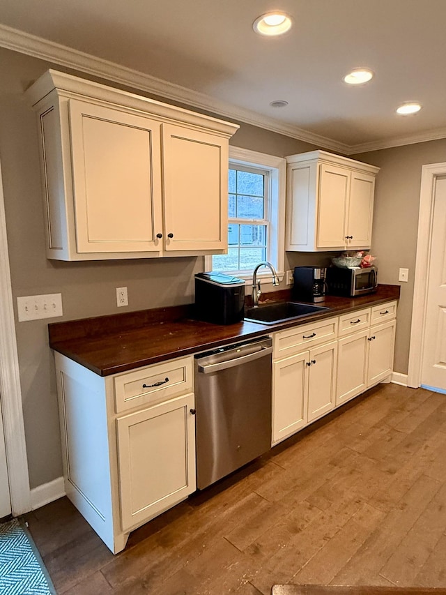 kitchen with stainless steel appliances, dark countertops, light wood-style floors, ornamental molding, and a sink