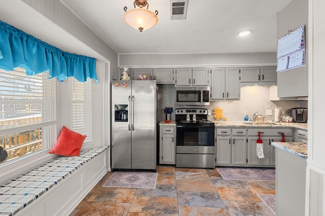 kitchen featuring visible vents, appliances with stainless steel finishes, a sink, gray cabinets, and backsplash