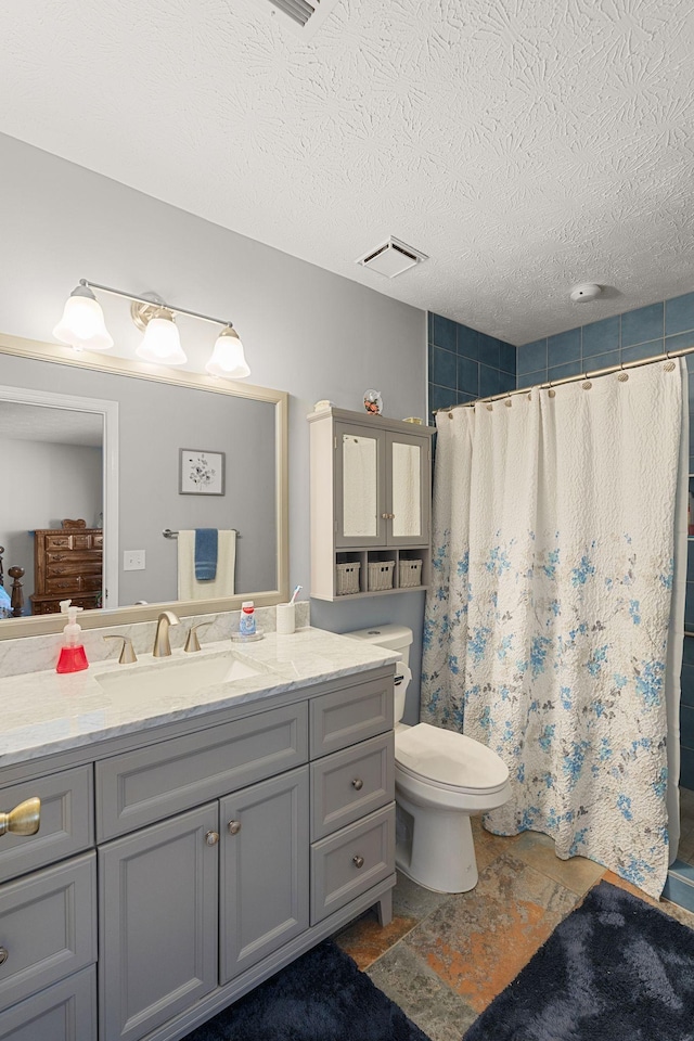 bathroom with a textured ceiling, toilet, vanity, visible vents, and a shower stall