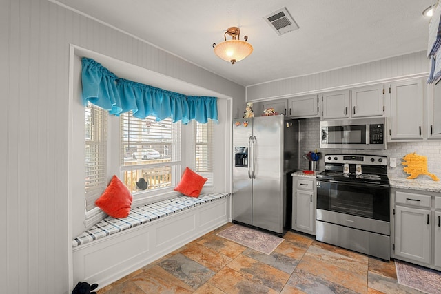 kitchen featuring tasteful backsplash, visible vents, gray cabinetry, appliances with stainless steel finishes, and stone finish floor