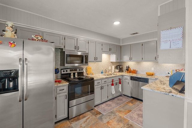 kitchen with decorative backsplash, appliances with stainless steel finishes, gray cabinets, stone tile flooring, and a sink