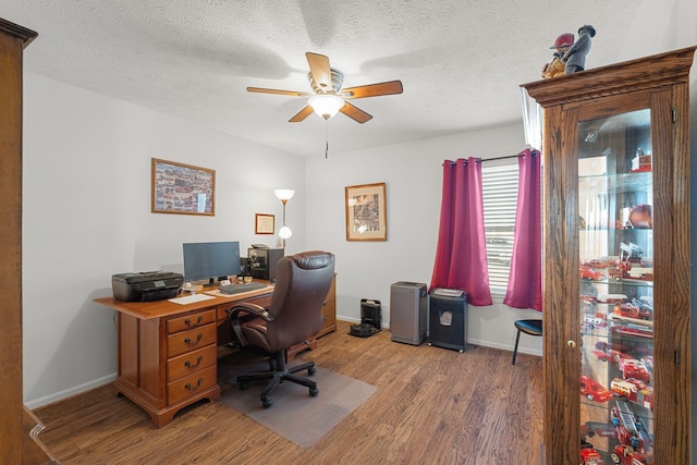 home office with a textured ceiling, wood finished floors, a ceiling fan, and baseboards