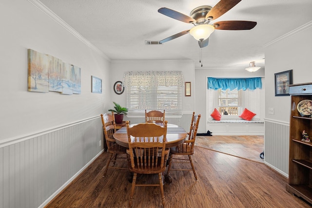 dining area with a wainscoted wall, crown molding, visible vents, a textured ceiling, and wood finished floors