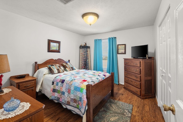 bedroom with a textured ceiling, dark wood-style flooring, and a closet