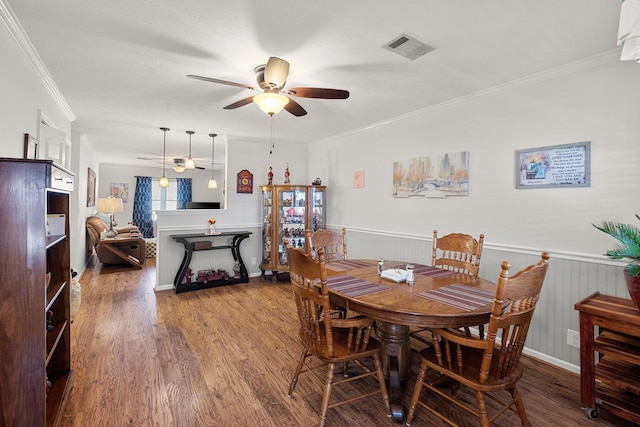 dining area featuring visible vents, ornamental molding, wainscoting, ceiling fan, and wood finished floors