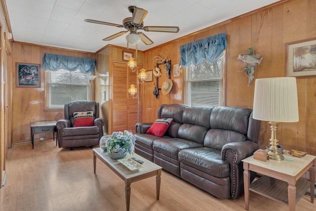 living area featuring plenty of natural light, ceiling fan, light wood-type flooring, and wooden walls