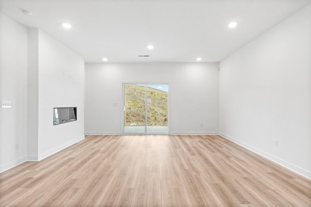 unfurnished living room with light wood finished floors, recessed lighting, visible vents, a glass covered fireplace, and baseboards