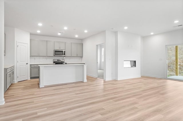 kitchen featuring gray cabinetry, open floor plan, light countertops, appliances with stainless steel finishes, and a center island with sink