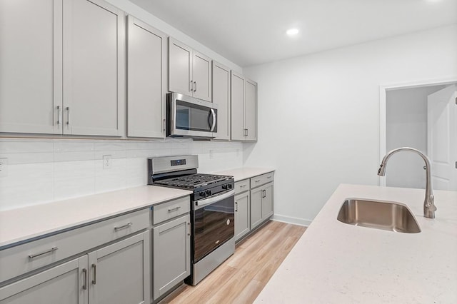 kitchen featuring light wood-style flooring, gray cabinetry, stainless steel appliances, a sink, and tasteful backsplash