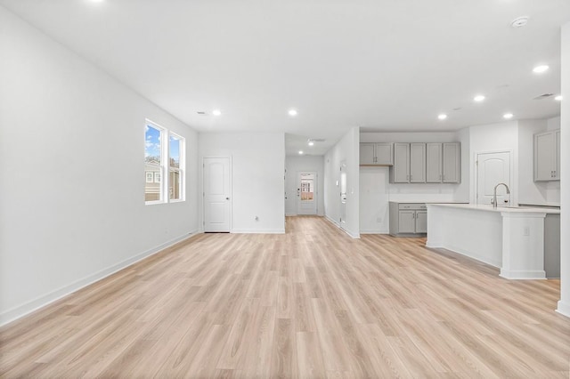 unfurnished living room featuring light wood-type flooring, a sink, baseboards, and recessed lighting