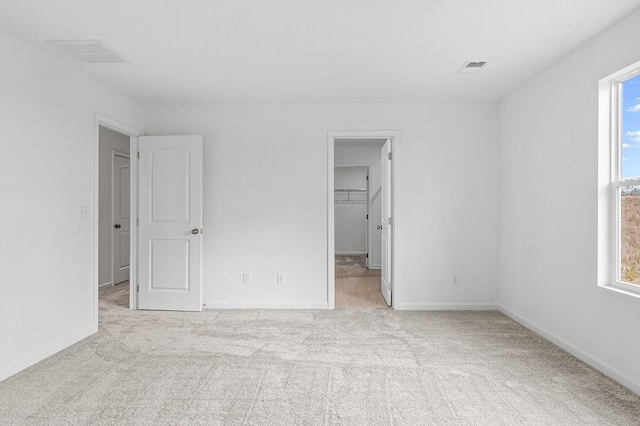 unfurnished bedroom featuring light carpet, a walk in closet, visible vents, and baseboards