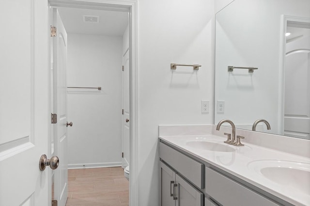 bathroom featuring double vanity, visible vents, toilet, wood finished floors, and a sink