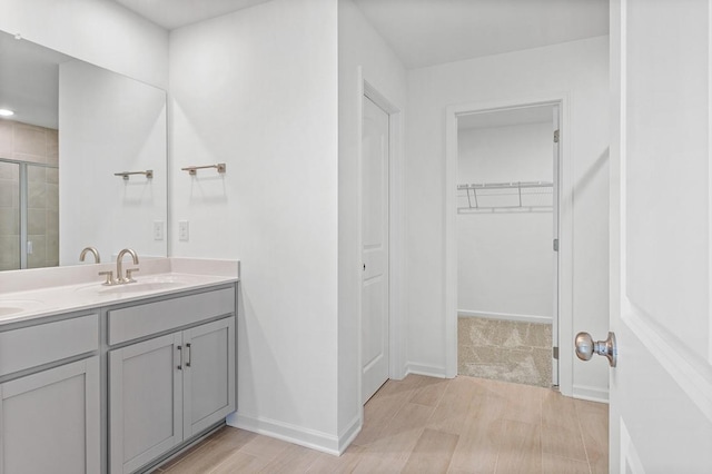 full bathroom with double vanity, a spacious closet, a sink, a shower stall, and baseboards