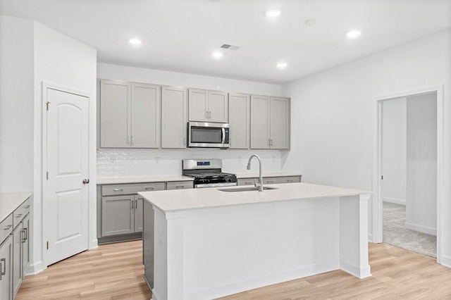 kitchen featuring light wood-style flooring, a kitchen island with sink, stainless steel appliances, light countertops, and a sink