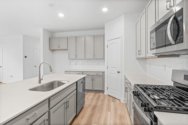 kitchen with light wood-style flooring, gray cabinets, stainless steel appliances, light countertops, and a sink