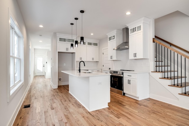 kitchen with wall chimney exhaust hood, light countertops, stainless steel range with electric cooktop, light wood-style floors, and a sink