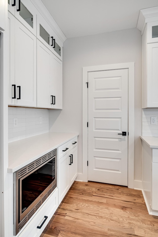 kitchen featuring light wood finished floors, decorative backsplash, glass insert cabinets, stainless steel microwave, and light countertops